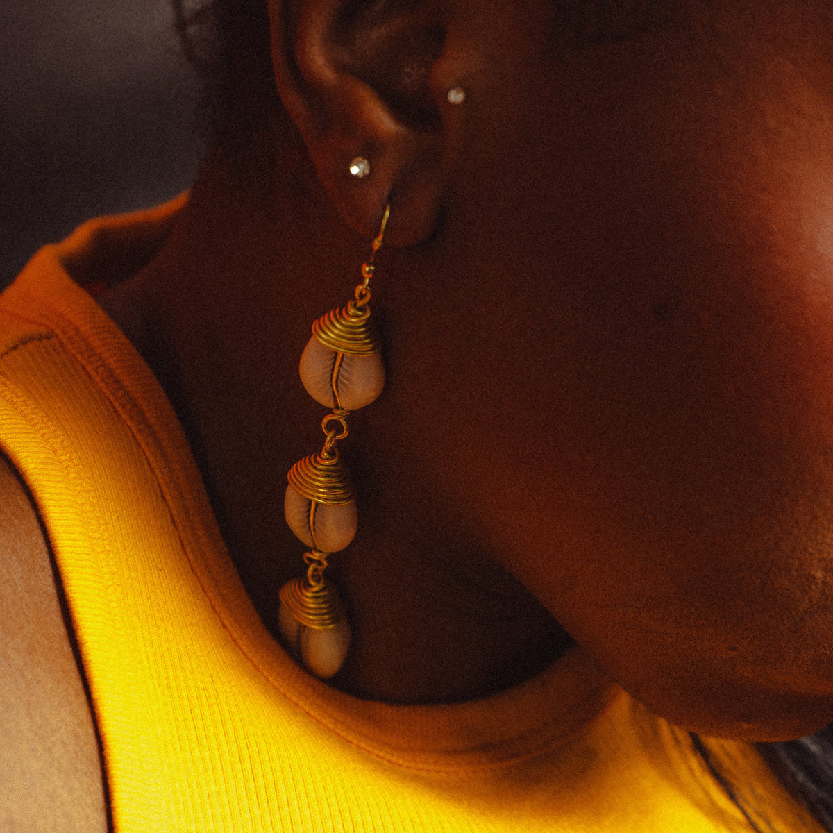 Boucles pendantes à trois cauris, portées, dans une lumière orangée
