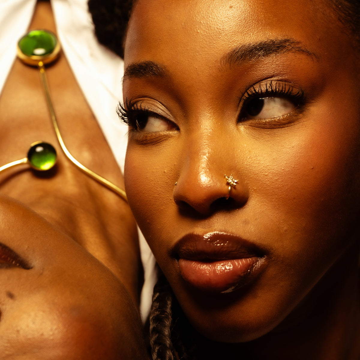 Gros plan du piercing de nez en fleur dorée, le collier à pierres vertes en arrière-plan