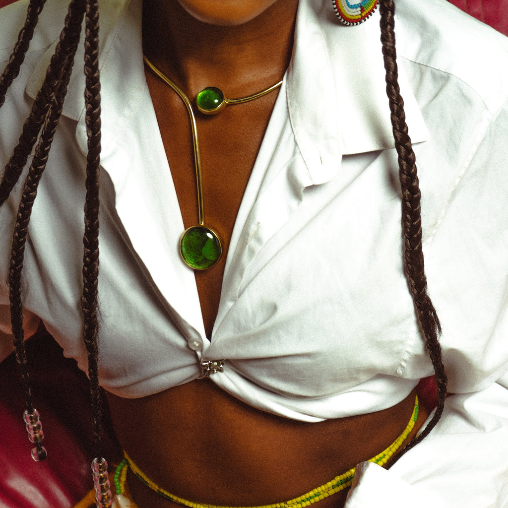 Collier asymétrique en laiton doré à deux pierres vertes, porté sur une chemise blanche nouée